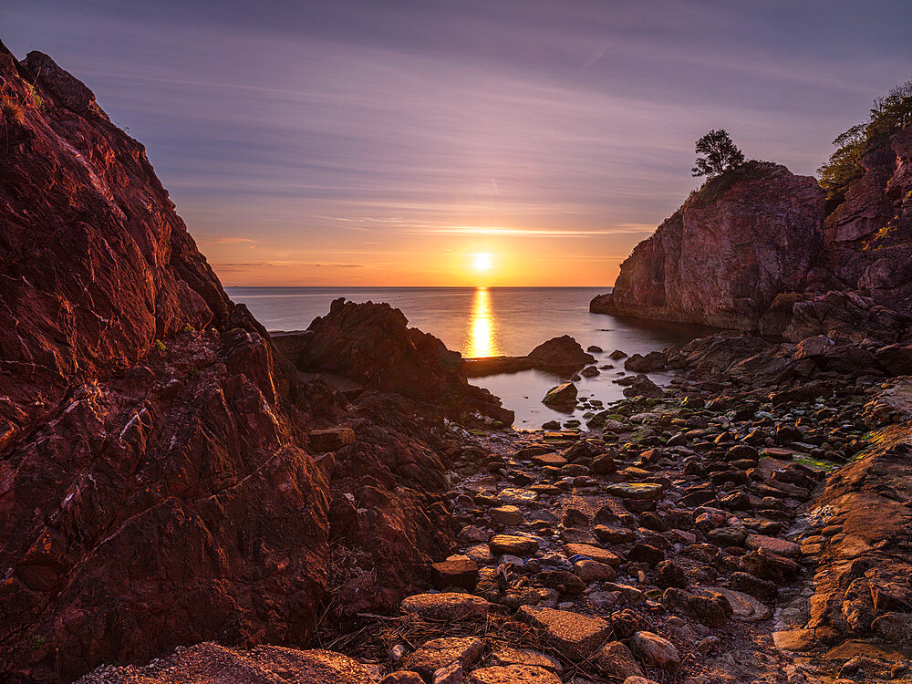 A colourful sunrise over Torbay with warm light on rocks, Babbacombe, Torquay, Devon, England, United Kingdom, Europe