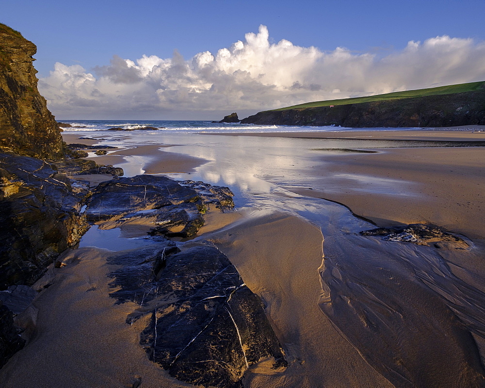 Atlantic clouds reflect dawn light onto the wet sands and rocks of Trevone, near Padstow, Cornwall, England, United Kingdom, Europe