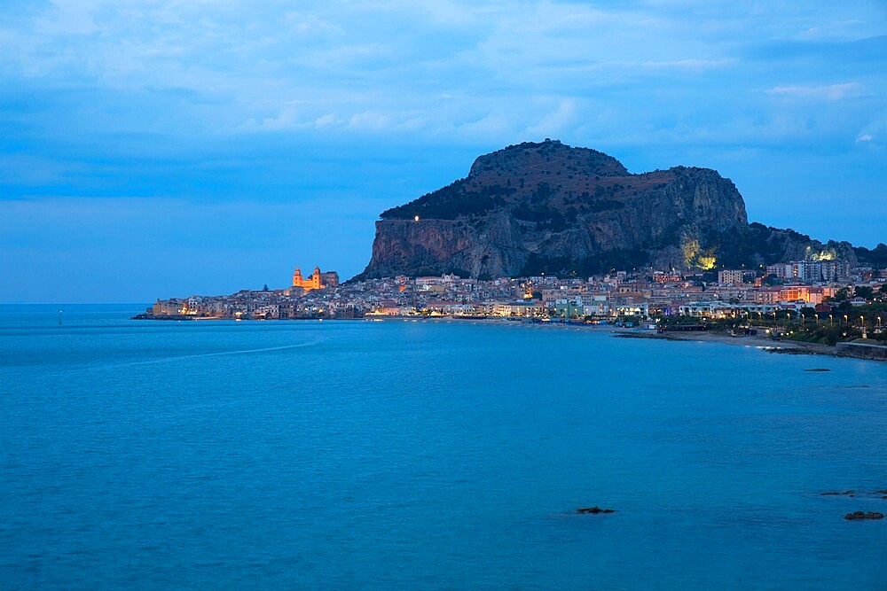 View along coast to the town and illuminated cathedral, dusk, La Rocca towering above, Cefalu, Palermo, Sicily, Italy, Mediterranean, Europe