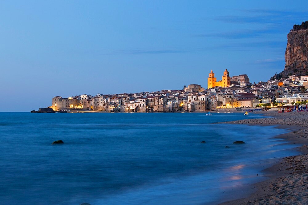 View along shore to the illuminated town and UNESCO World Heritage Site listed Arab-Norman cathedral, dusk, Cefalu, Palermo, Sicily, Italy, Mediterranean, Europe