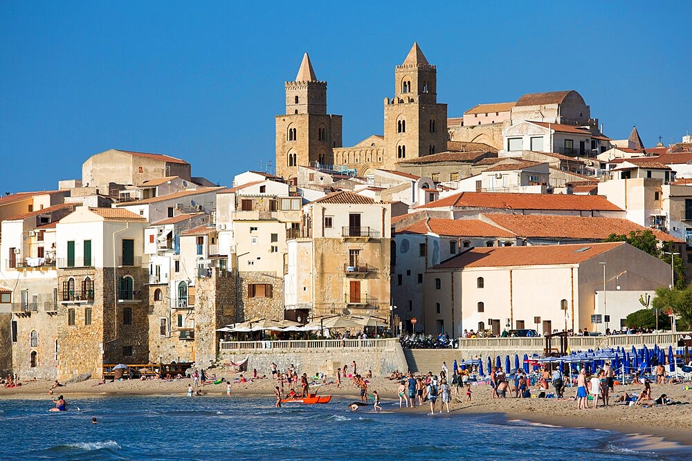 View from beach along water's edge to the town and UNESCO World Heritage Site listed Arab-Norman cathedral, Cefalu, Palermo, Sicily, Italy, Mediterranean, Europe