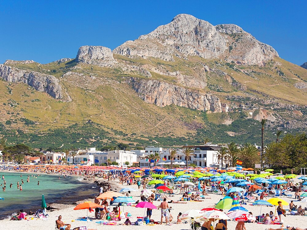 View across colourful crowded beach to the rugged slopes of Pizzo di Sella, San Vito Lo Capo, Trapani, Sicily, Italy, Mediterranean, Europe