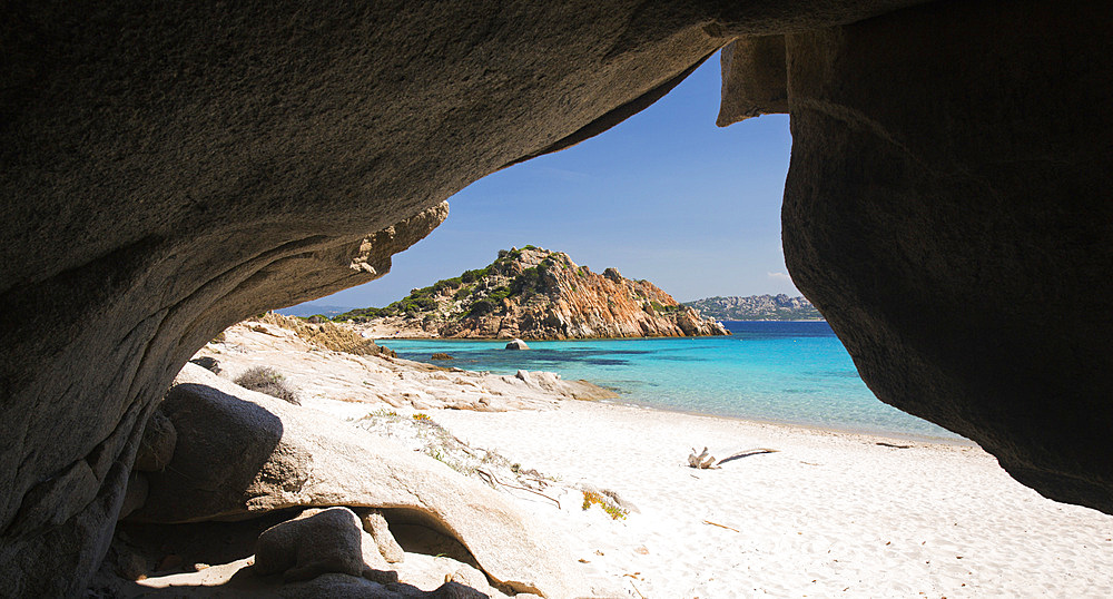 View through cave entrance across the clear turquoise waters of Cala Corsara to the pink granite headland of Punta Rossa Corsara, Spargi Island, La Maddalena Archipelago National Park, Sassari, Sardinia, Italy, Mediterranean, Europe