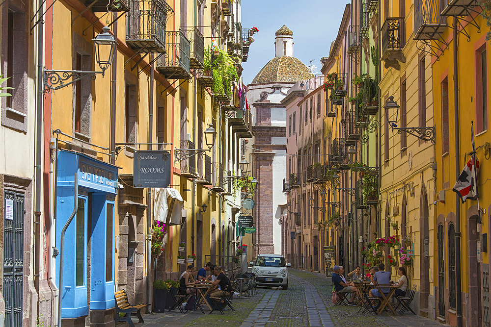 View along cobbled Corso Vittorio Emanuele II in the historic Sa Costa district, colourful tiled dome of the Cathedral prominent, Bosa, Oristano, Sardinia, Italy, Mediterranean, Europe