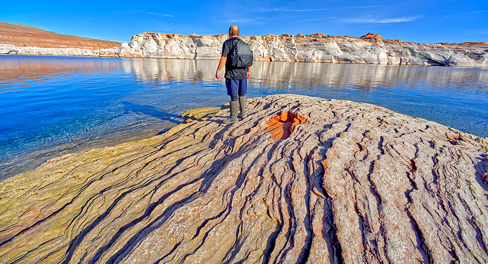 Man hiking along rocky shoreline of Lake Powell in an area called the Chains in the Glen Canyon Recreation Area, Page, Arizona, United States of America, North America