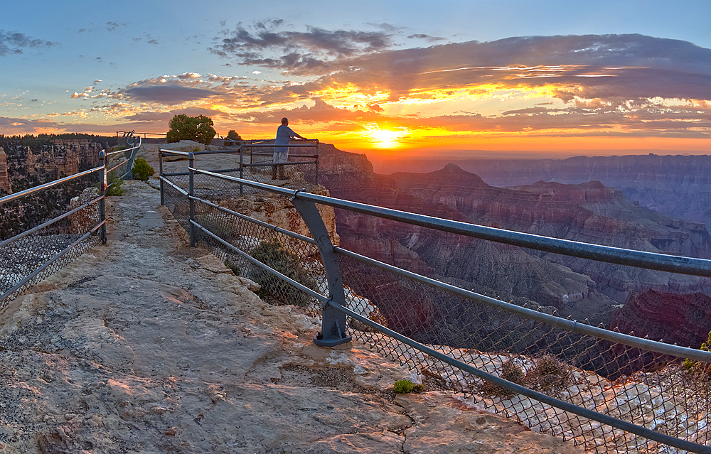 A lone hiker on Angels Window Overlook at Grand Canyon North Rim Arizona looking out at the sunrise.