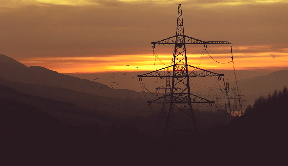 Striking pylons run through a hazy sunset in the Peak District, South Yorkshire, Yorkshire, England, United Kingdom, Europe