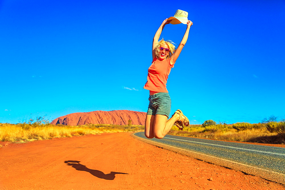 Tourist woman jumping and holding her hat at Uluru (Ayers Rock) in Uluru-Kata Tjuta National Park, UNESCO World Heritage Site, Northern Territory, Central Australia, Pacific