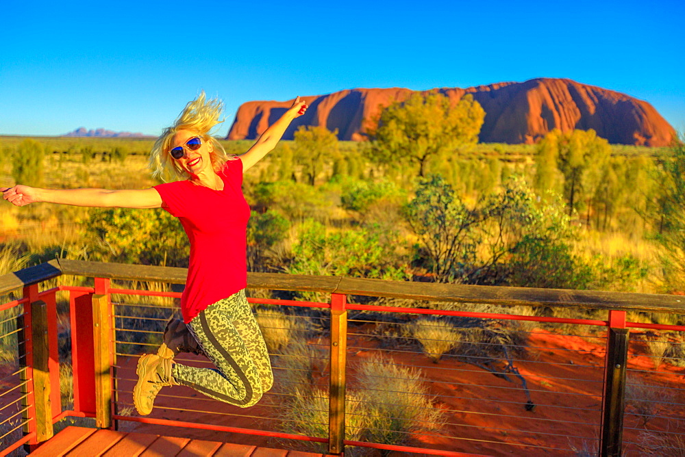 Tourist woman jumping in Uluru-Kata Tjuta National Park, UNESCO World Heritge Site, with Uluru and Kata Tjuta in the background, Northern Territory, Australia, Pacific