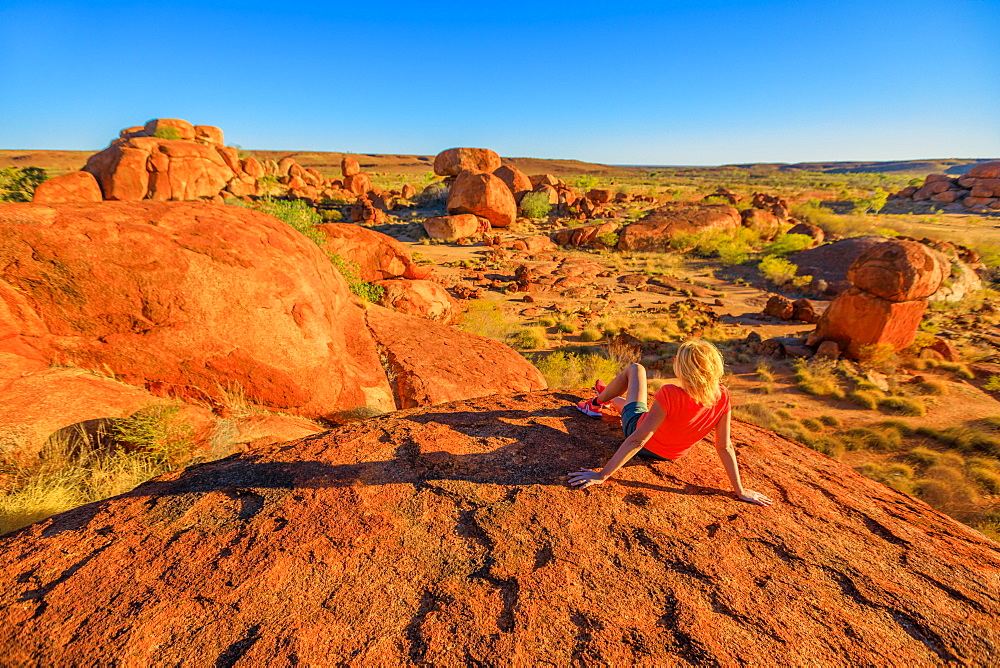 Tourist woman on the top view of Karlu Karlu (Devils Marbles) Conservation Reserve looking at panorama of granite boulders and rock formations at sunset, Outback, Northern Territory, Australia, Pacific