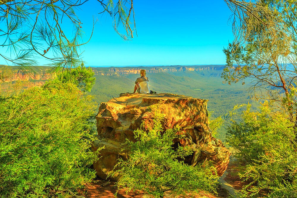 Tourist woman relaxing after hiking and enjoying panoramic views of granite boulders rock formations from Baltzer Lookout in Blue Mountains National Park near Sydney, New South Wales, Australia, Pacific