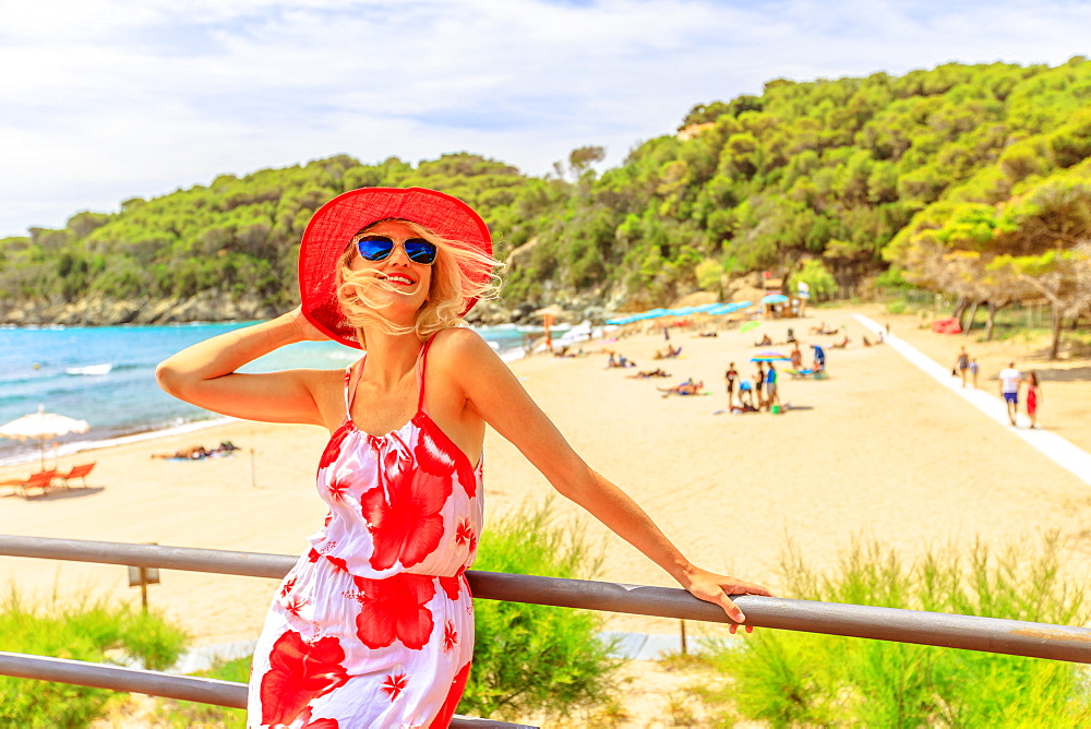 Happy woman tourist with wide red hat on roof top at Fetovaia Beach, Elba island, Tuscany, Italy, Europe