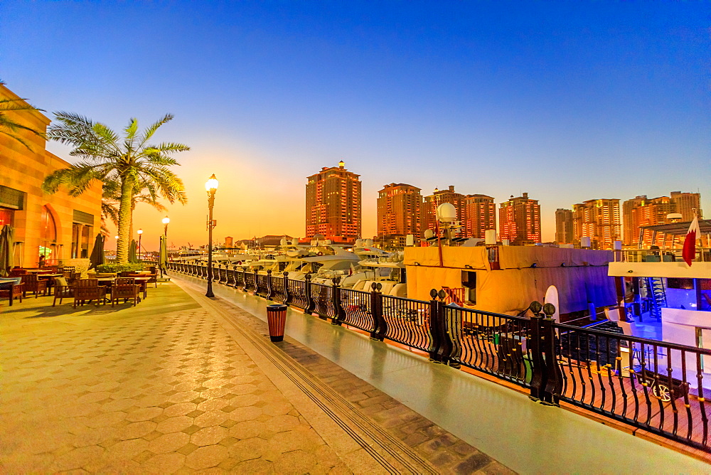 Marina corniche promenade at night in Porto Arabia at the Pearl-Qatar, with residential towers and luxury boats and yachts in Persian Gulf, Doha, Qatar, Middle East