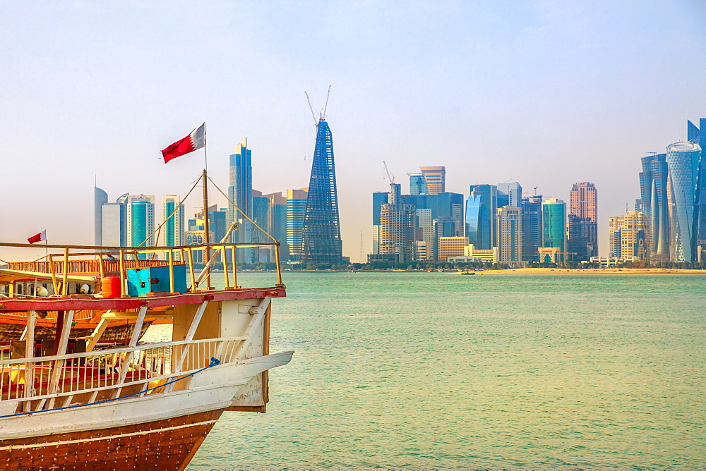 Close up of traditional wooden dhow with Qatari flag in Doha Bay in foreground and skyscraper towers of West Bay skyline in background, Doha, Qatar, Middle East