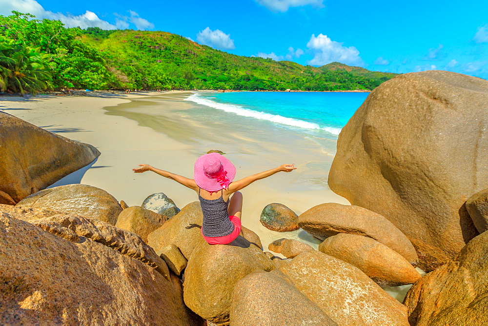 High angle view of bay of Anse Lazio with tourist woman in pink hat sitting above a rock formations at Lazio beach, Praslin Island, Seychelles, Indian Ocean, Africa