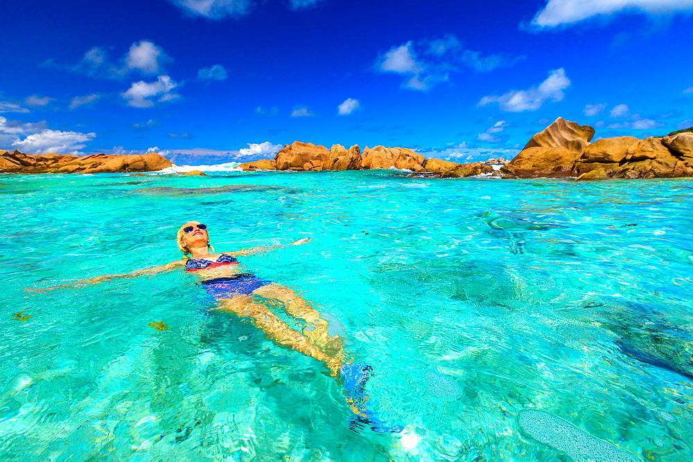 Swimming pool at Anse Cocos with woman in bikini lying in turquoise water of natural pool at Anse Cocos Beach protected by rock formations, La Digue, Seychelles, Indian Ocean, Africa