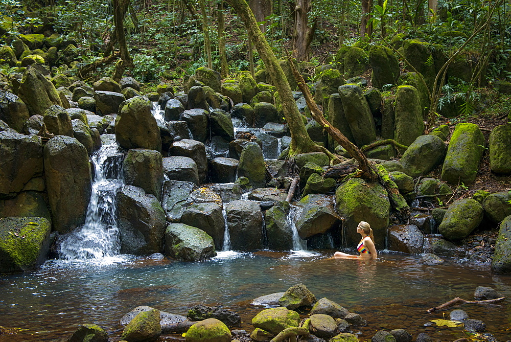 Woman lounging in a pool beneath a waterfall in Kauai, Hawaii, United States of America, North America