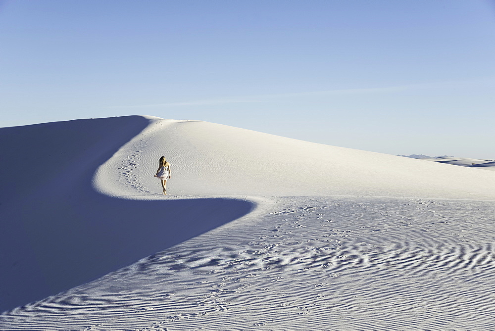 Woman walking along a white sand dune, cast in blue late-afternoon light, in White Sands National Monument, New Mexico, United States of America, North America