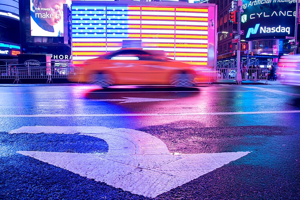 Taxi blurring by an illuminated flag of the United States of America at Times Square, New York City, United States of America, North America