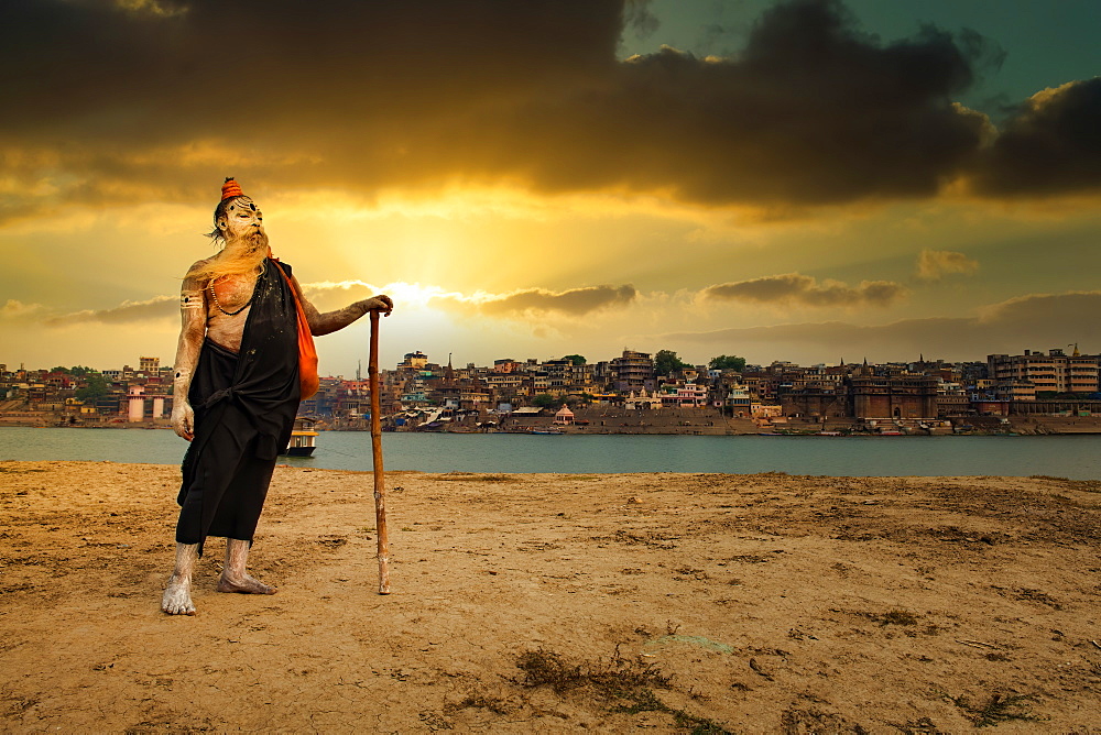 An Indian Hindu Sadhu (saint) on the banks of holy river of Ganges and Varanasi city in the background, Varanasi, Uttar Pradesh, India, Asia