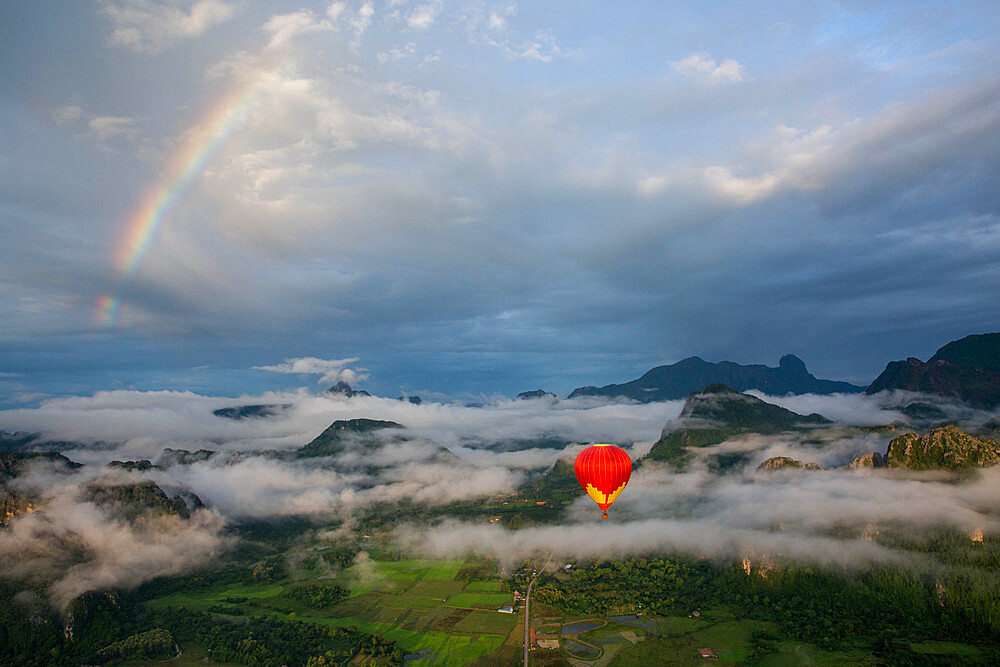 A sunrise over Vang Vieng, with a rainbow over the clouds, as a hot air balloon rises in the foreground, Laos, Indochina, Southeast Asia, Asia