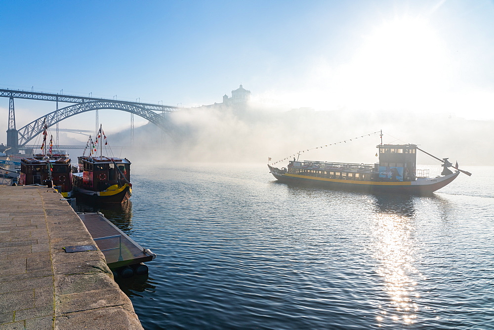 Boat sailing down the River Douro in early morning mist with Dom Luis I Bridge in background, Porto, Portugal, Europe