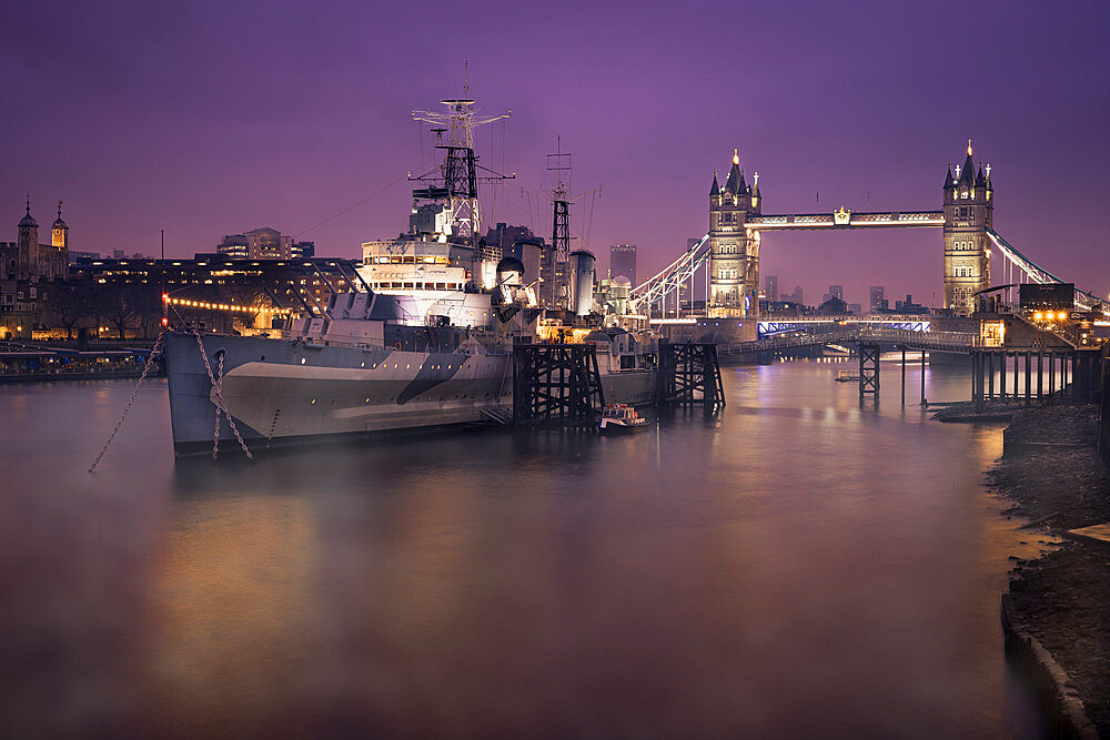 HMS Belfast with Tower Bridge in background, shot early morning with Thames Mist and city lights, London, England, United Kingdom, Europe