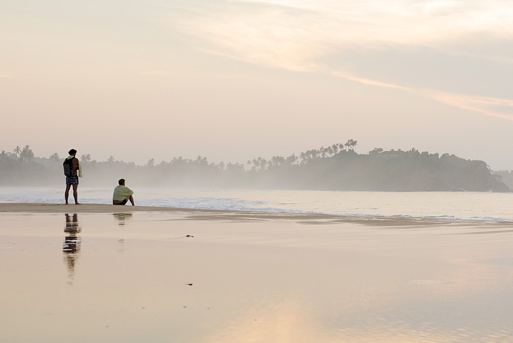 Two men watching the sunrise on Talalla beach, Sri Lanka, Asia