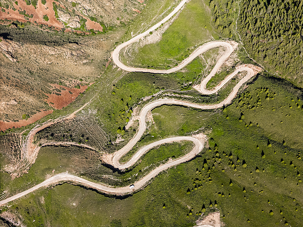 Aerial view of a winding mountain road curves, Kalmak Ashuu Pass, through lush greenery in Kyrgyzstan, Central Asia, Asia