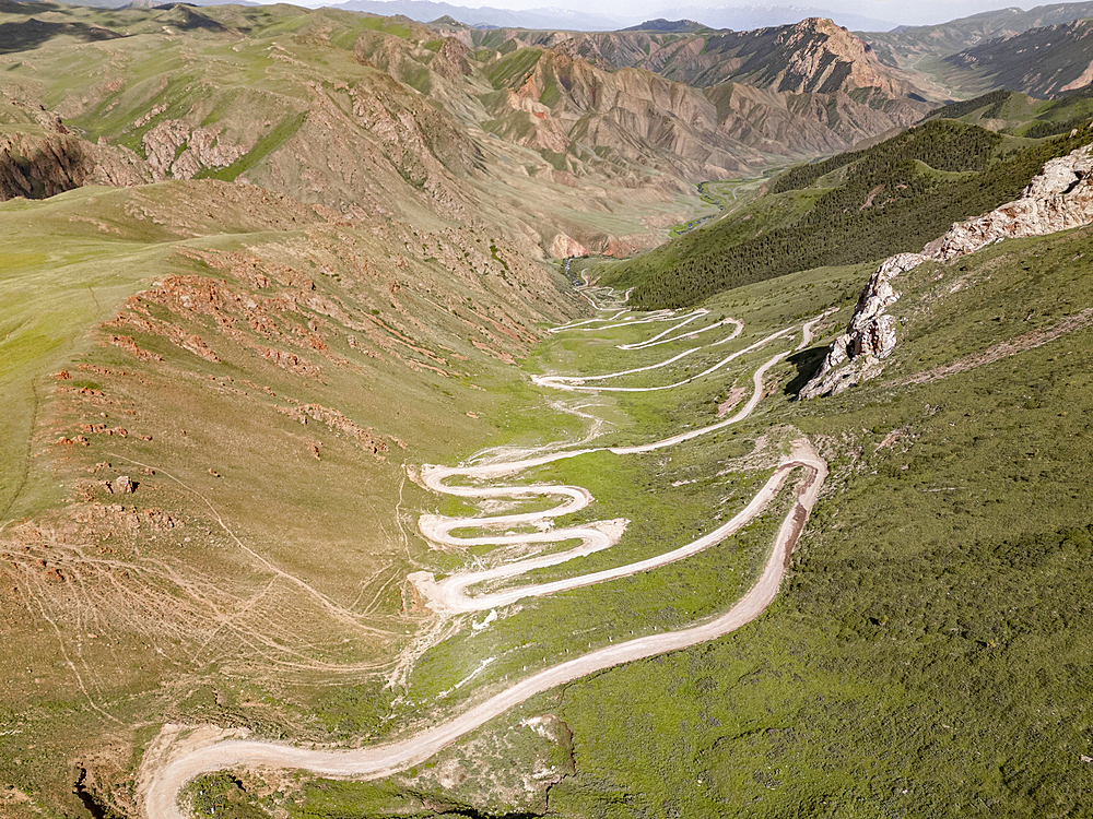 Aerial view of a winding mountain road curves, Kalmak Ashuu Pass, through lush greenery in Kyrgyzstan, Central Asia, Asia