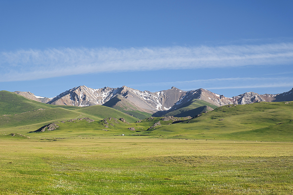 Vast green meadows meet majestic mountains at Song-Kol Lake in Kyrgyzstan under a clear blue sky