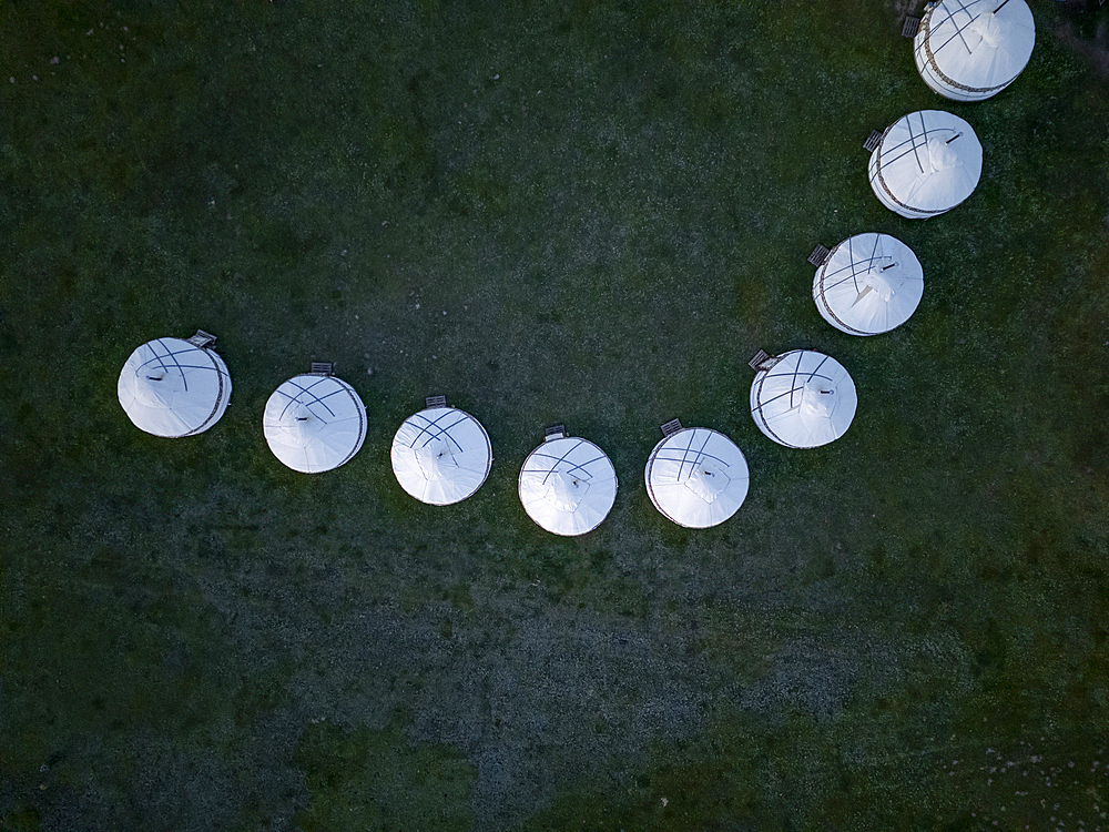 Line of white yurts in a curved pattern on grassy plain, viewed from above, near Song Kol Lake, Kyrgyzstan