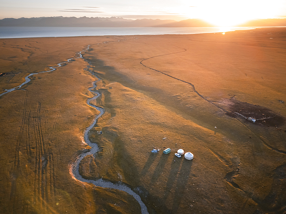 An aerial view of Son Kol lake area in Kyrgyzstan during sunrise, showcasing the meandering river and a small camp with tents