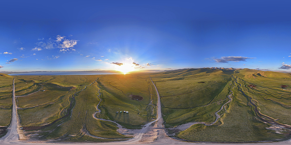 A stunning panoramic 360° view of Song Kol lake in Kyrgyzstan, captured during a beautiful sunrise. The vibrant colors of the sky, the lush green fields, and the winding roads create a truly breathtaking scene