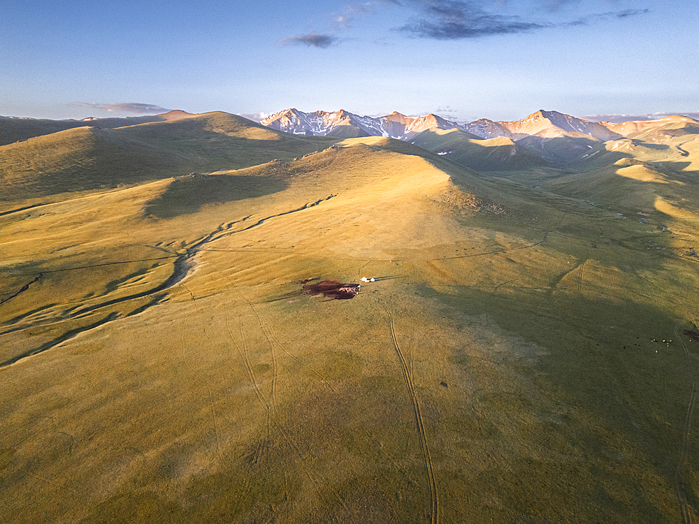 A view of the Song Kol Lake area in Kyrgyzstan, with a few yurts nestled in the foothills of the mountains at sunrise