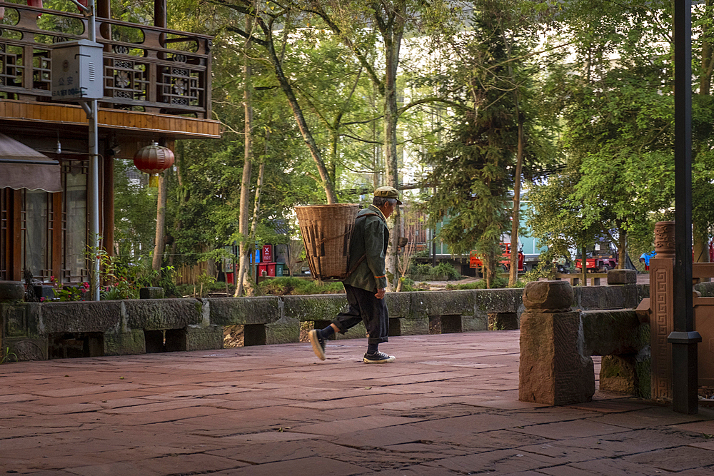 A man with a wicker basket on his shoulders walking at dawn through Shangli town