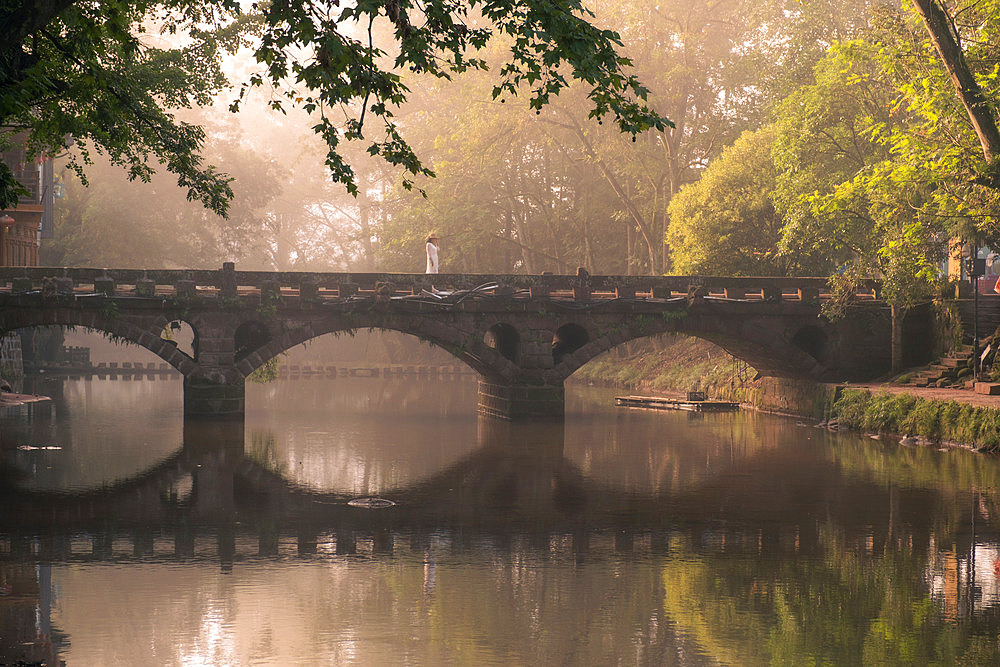 An ancient stone bridge in Shangli Town reflected in the river shrouded in morning mist.