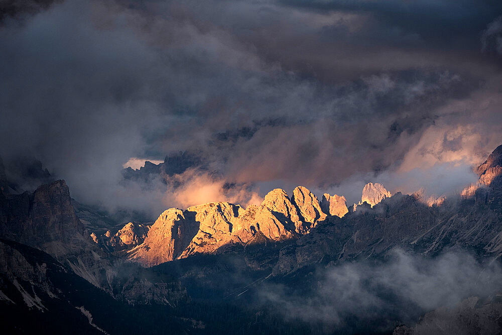 Light rays hitting Dolomites mountain peaks at sunset, surrounded by low clouds and mist, Cortina d'Ampezzo, Dolomites, Veneto, Italy, Europe