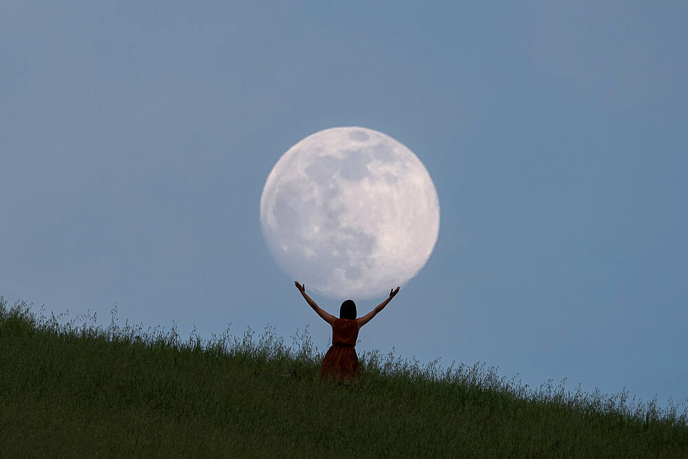 Full moon portrait at blue hour with a girl holding the moon above her head, Emilia Romagna, Italy, Europe