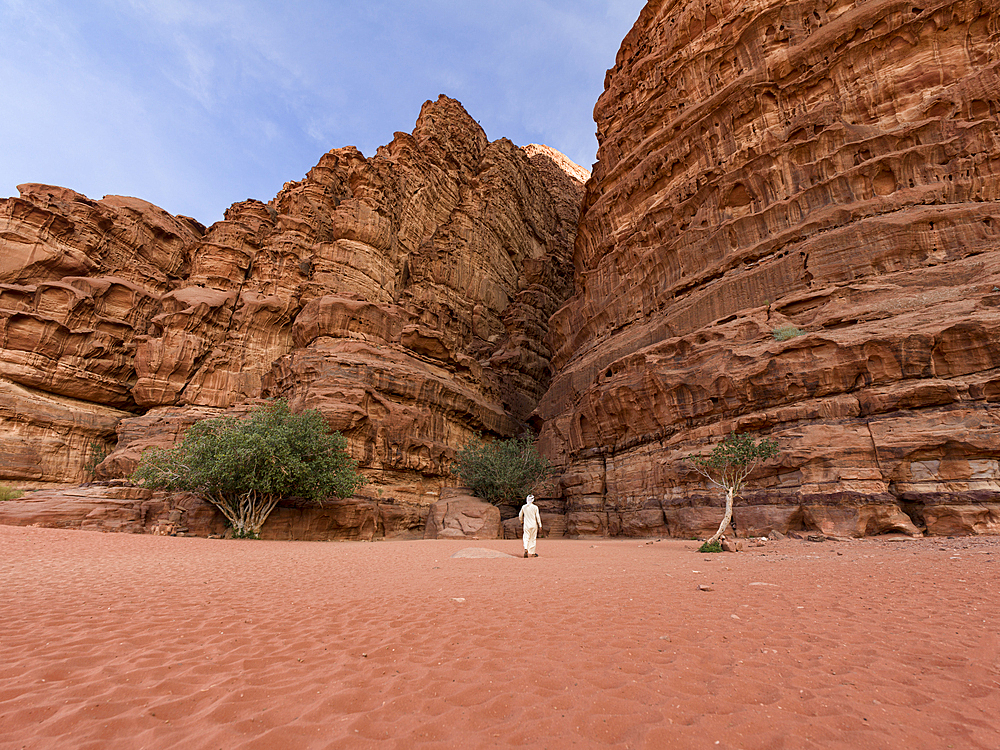 A beduin with traditional white clothes walking towards a canyon in Wadi Rum desert in Jordan