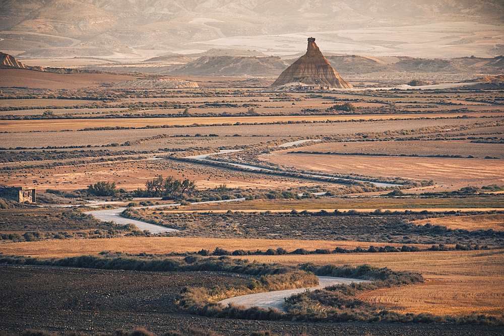 The badlands of Bardenas Reales at sunrise with a winding road leading towards the Castildetierra rock formation, Navarre, Spain, Europe