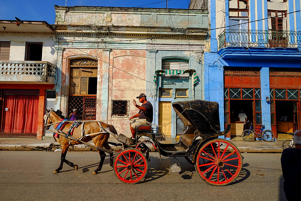 A horse-drawn carriage driver waves as he passes by, Cardenas, Matanzas, Cuba, West Indies, Central America