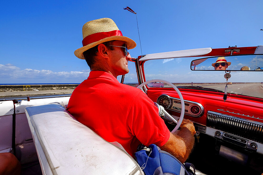 Man in straw hat drives vintage car along the Malecon, Havana, Cuba, West Indies, Central America