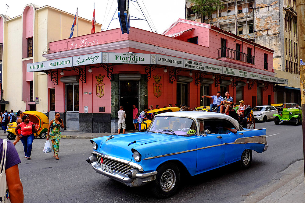 Pedestrians, vintage cars, and a horse-drawn carriage travel past Floridita on the streets of Havana, Havana, Cuba, West Indies, Central America