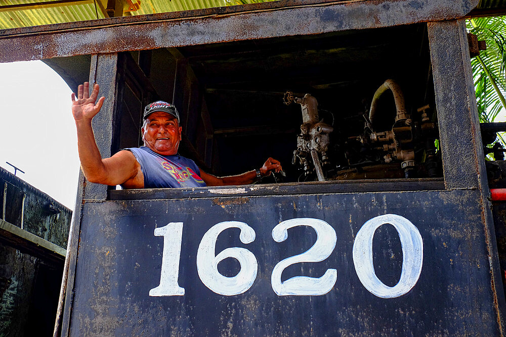 A smiling man waves from the engine of a train, Cienfuegos, Cuba, West Indies, Central America