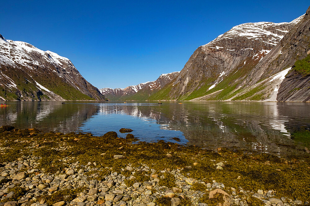 Snow capped mountains reflected in the still waters of the fjord where kayakers are enjoying the view, Nordfjord, Norway, Scandinavia, Europe