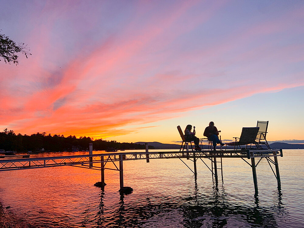 Mother and daughter play ukulele's together on a dock over Sebago Lake, Maine, United States of America, North America