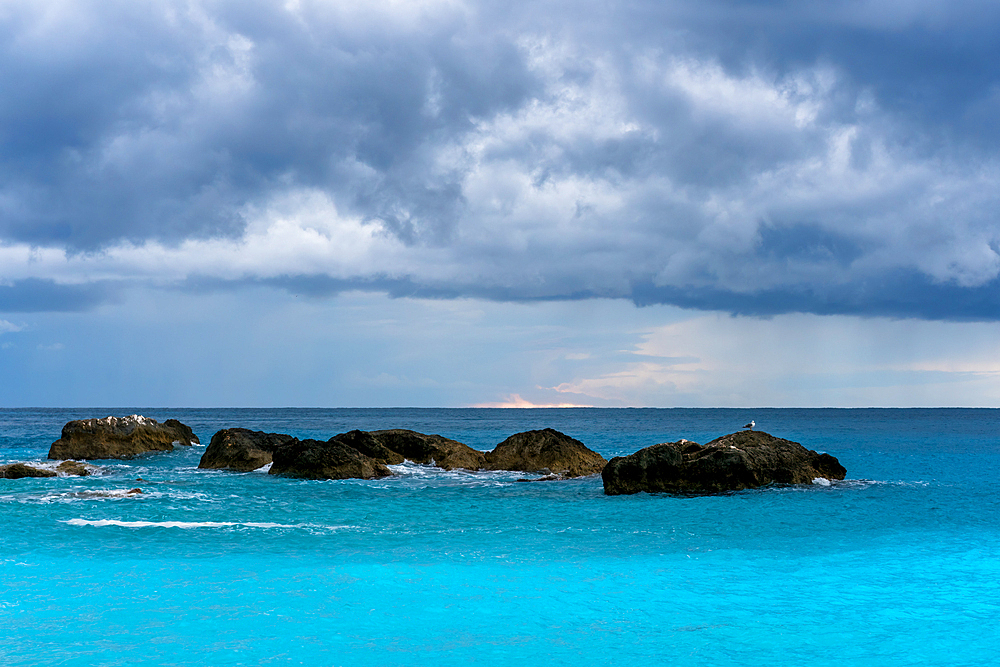 Seagulls on top of rocks on the middle of a turquoise water sea in Greece on a stormy day