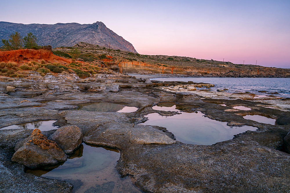 Aspes beach natural holes on the rocks full with water at sunset with turquoise water sea of Greece on the background