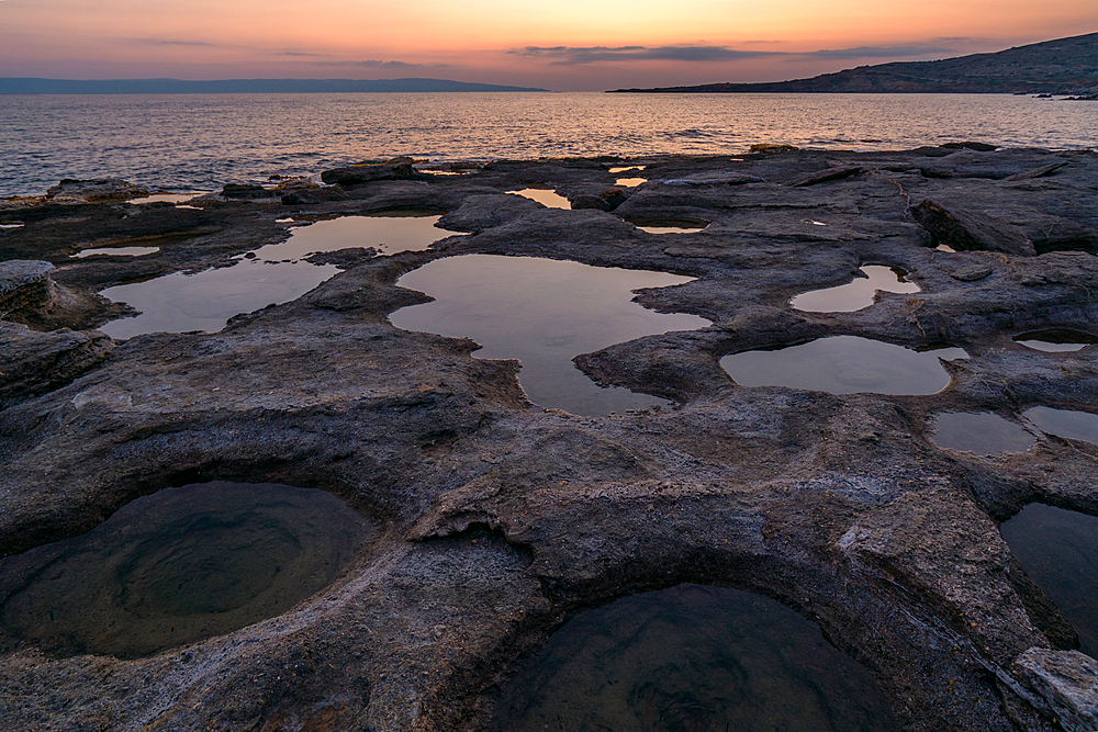 Natural holes on the rocks full with water at sunset with turquoise water sea of Greece on the background